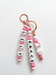 Handcrafted, personalized charm made from BPA-free soft silicone in shades of pink and white. It features three strands: two with name beads and one with a cute white llama figurine with a pink rose, all attached to an elegant rose gold clasp.