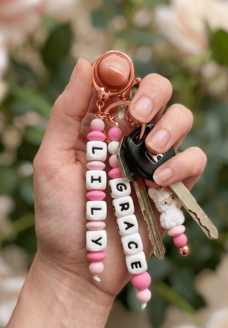A stylish and practical baby accessory: a personalized name charm attached to a diaper bag on a stroller. The product combines identity and aesthetic design, perfectly matching modern nursery and parenting gear.