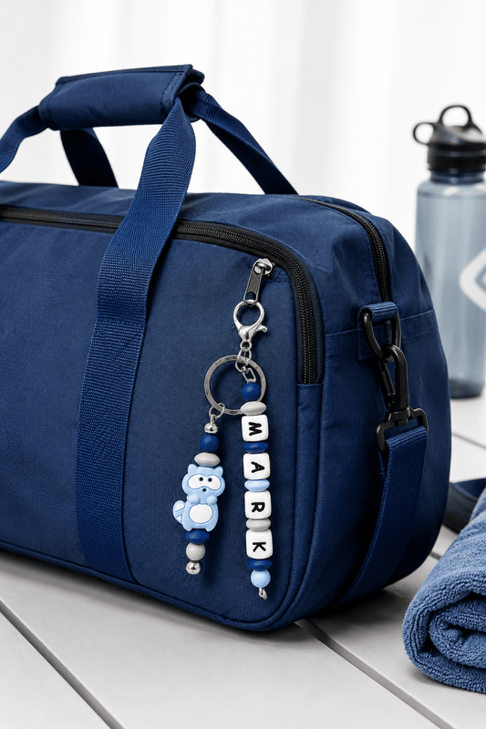 Personalised boys backpack charm with custom name, handmade silicone bead keychain in blue and black, clipped onto a school bag.