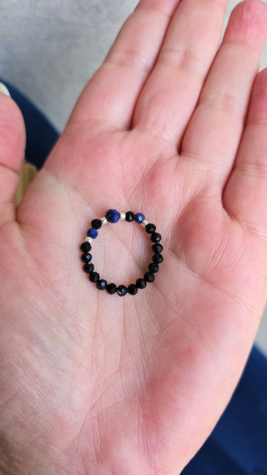 Three handmade elastic gemstone rings with Lapis Lazuli, Black Tourmaline and Moonstone beads, featuring gold and silver accents on a minimalist background.