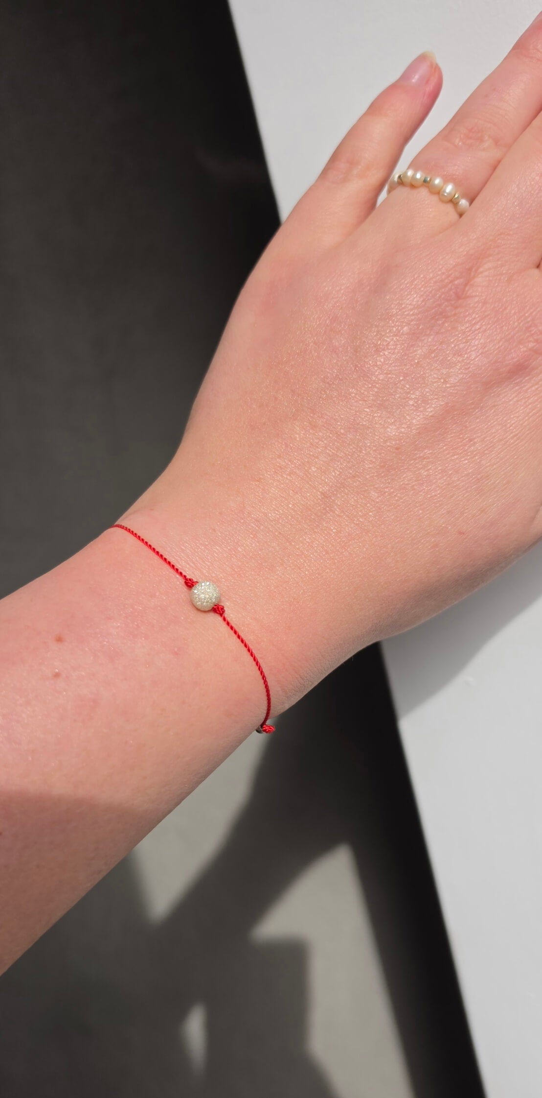 Close-up of a 6mm stardust effect sterling silver bead showing diamond-like sparkle on red cord.