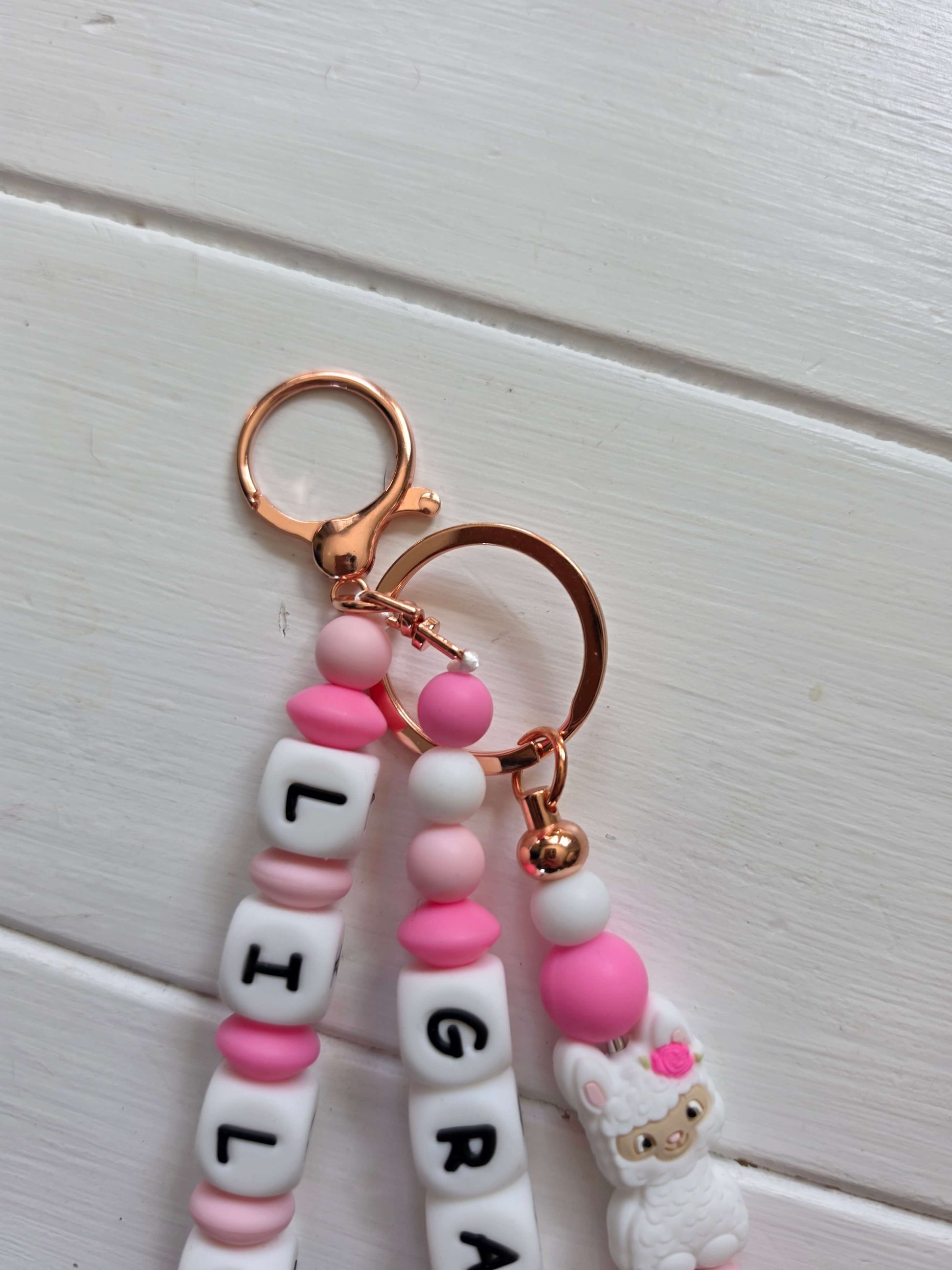 An elegant close-up of a personalized name charm held in hands against a soft, floral background. A perfect baby shower gift idea that grows with the child, transitioning from a pram accessory to a school backpack charm.