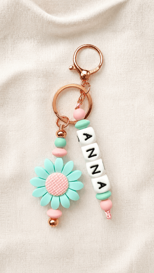 Product on linen background
Personalised silicone bag charm with custom name letter beads, pastel pink and mint beads, rose-gold hardware and daisy flower charm displayed on a soft neutral linen background.