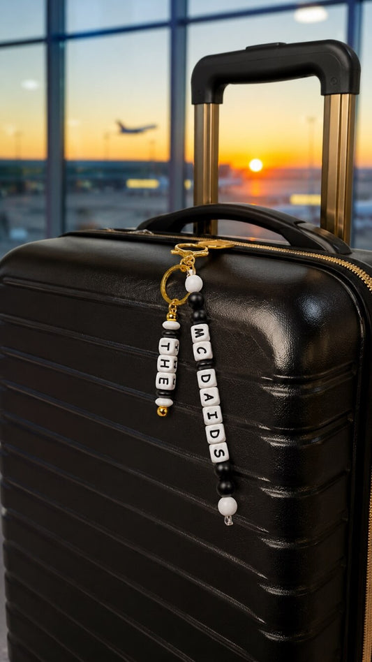 Personalised black and white silicone bead luggage tag with gold-tone hardware attached to a suitcase, custom family name travel accessory.
