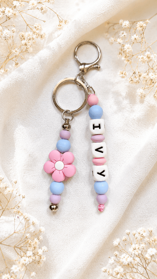 Elegant silicone bag charm with purple, blue and soft pink beads and silver-tone hardware on a soft cream background.
