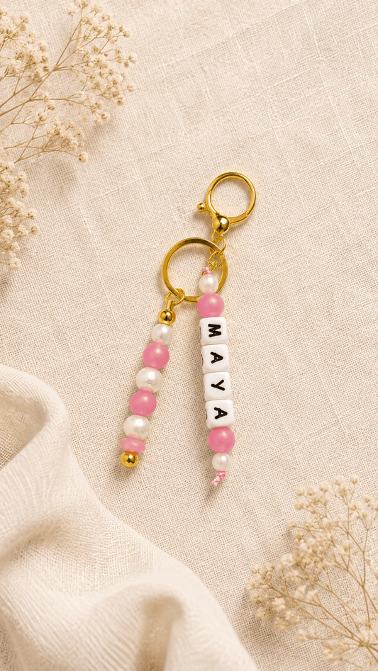 Elegant silicone bag charm with pearl and soft pink beads and gold-tone hardware on a soft cream background.