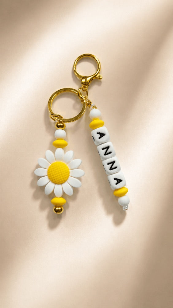 Personalised daisy keychain with custom name ANNA, white and yellow silicone beads and gold-tone ring attached to a set of keys.
