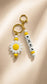 Personalised daisy keychain with custom name ANNA, white and yellow silicone beads and gold-tone ring attached to a set of keys.

