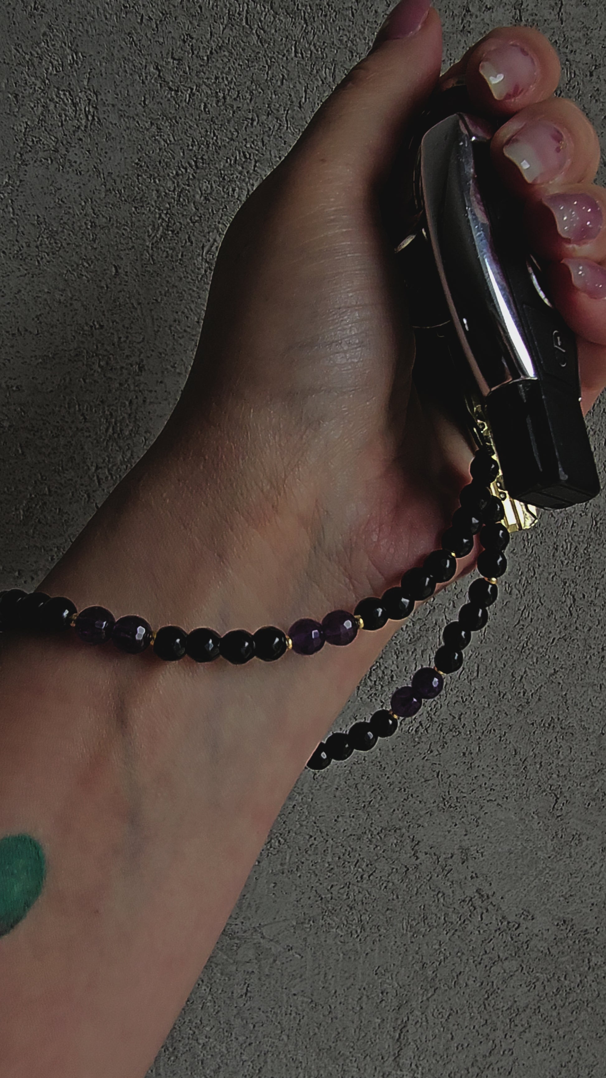 Handmade crystal phone charm with black onyx and amethyst beads, gold accents, and a cord – used as a protective and calming accessory.