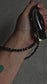Handmade crystal phone charm with black onyx and amethyst beads, gold accents, and a cord – used as a protective and calming accessory.