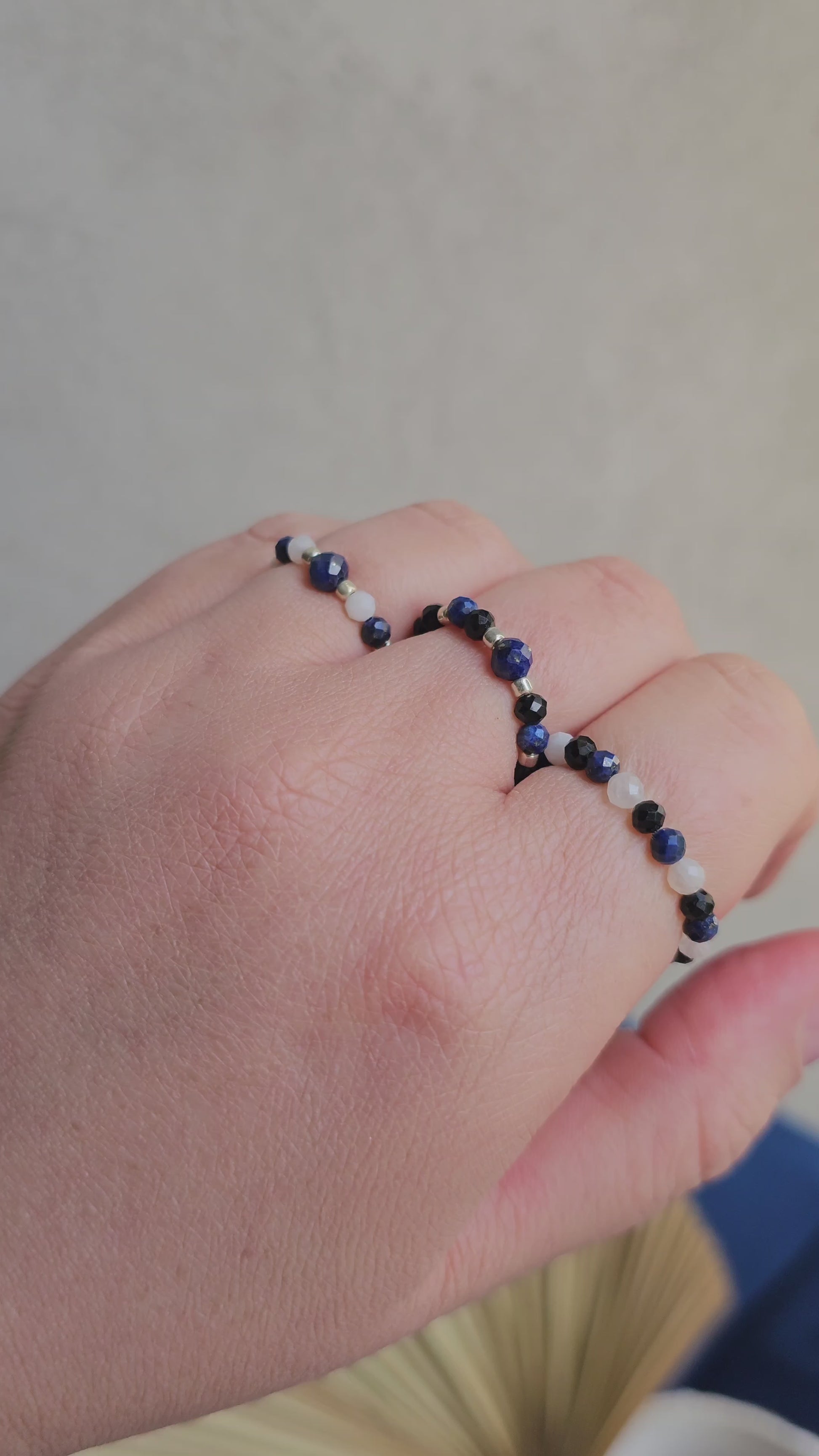 Three handmade elastic gemstone rings with Lapis Lazuli, Black Tourmaline and Moonstone beads, featuring gold and silver accents on a minimalist background.